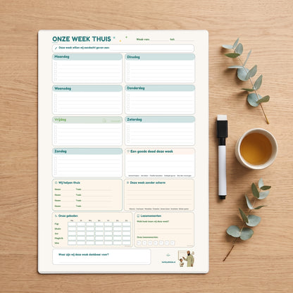 Onze Week Thuis magneetplanner op tafel met marker en een kop thee